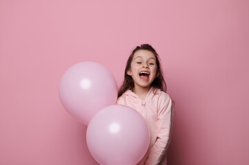 Obraz na płótnie Canvas Caucasian beautiful little child, birthday girl in pink clothes, laughing looking at camera, posing with pink pastel helium balloons, isolated over pink color background with copy advertising space