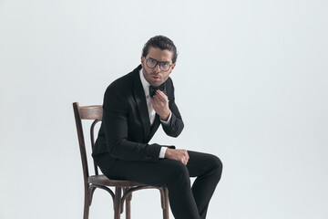 side view of cool elegant man with glasses sitting and adjusting bowtie