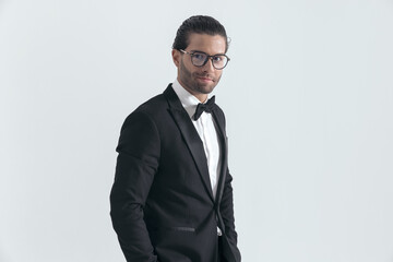 handsome elegant groom with glasses posing with hands in pockets
