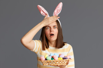 Indoor shot of frighten astonished woman wearing rabbit ears holding colorful Easter eggs isolated...