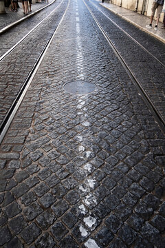 detail of the cobblestone floor of a street in lisbon with the tramway tracks in the Alfama district, a manhole cover in the middle of the street, vertical