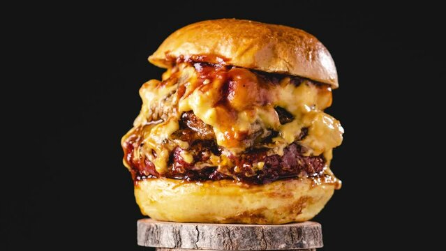 Big pulled pork and beef burger with many cheese and bbq sauce rotating con dark background