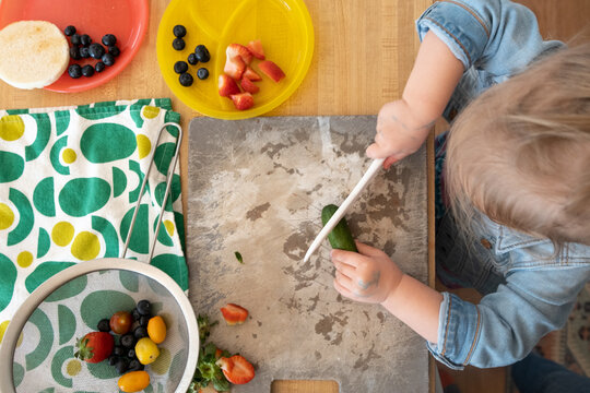 Picky Toddler Learns To Prepare Her Own Food; Teaching Child To Cut Soft Foods With A Plastic Knife