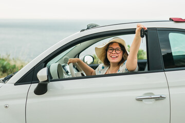 Car driver woman smiling showing new car keys and car. Female driving rented cabrio on summer...