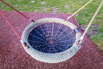 Close up of birds nest children's play swing hanging from rope in outdoor playground with soft floor
