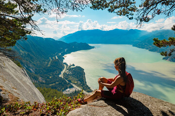 Naklejka na ściany i meble Hiking woman hiker in sitting looking at view of amazing nature landscape on famous Squamish Stawamus Chief Mountain Hike, British Columbia, Canada. Popular outdoor activity destination in Canada