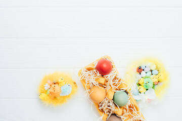 Painted multi-colored eggs in a yellow cardboard tray on a white wooden background. Easter background, symbol