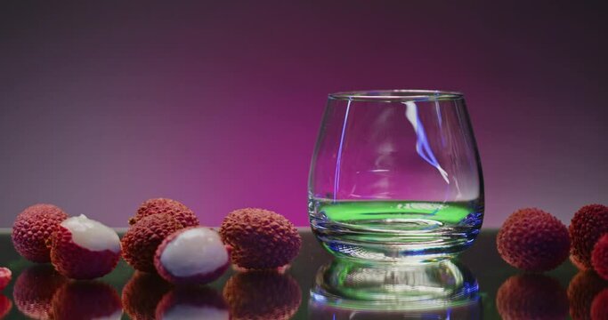 Green cocktail with syrup. Stock clip. Pink background with backlight next to the lying lychee and pouring a bright drink.