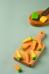 Candies, marzipan carrots handmade from colored marzipan on a wooden mini board on a plain green vinyl background.