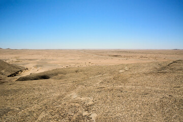Arid desert hills with rocks all the way to the horizon against a blue sky background