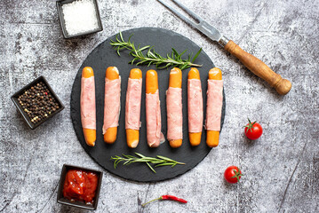 raw sausages wrapped in bacon on a stone background