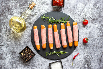 raw sausages wrapped in bacon on a stone background