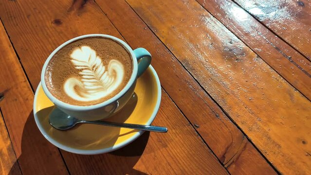 4k clip with speciality coffee cup with art latte depicting a flower served on a yellow table