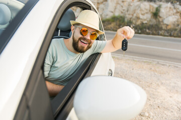 Car driver man smiling showing new car keys and car. Bearded guy driving rented cabrio on summer...