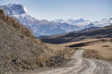 Road in the autumn mountains against the backdrop of a rocky ridge of mountain peaks with the first snow, sunny autumn day in the mountains landscape