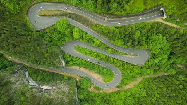 Aerial view of a winding road in the mountains, shot from a drone from a higher altitude and a low camera angle for a top view. Video of a serpentine road in the mountains in Bicaz area, Romania.