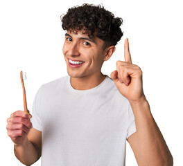 A young latin man brushing with a wooden teethbrush having an idea, inspiration concept.
