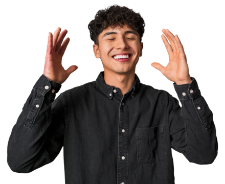 Young latin man praying for luck, amazed and opening mouth looking to front.