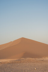 Fototapeta na wymiar Golden yellow sand dune in contrast with soft blue sky in the dry hot desert