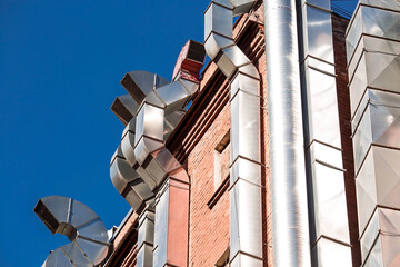 Large shiny ventilation pipes on the brick wall on the outside of the building.