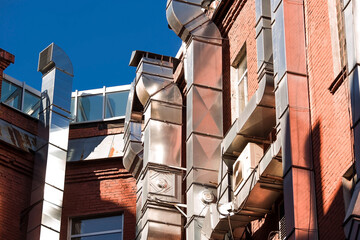 Large shiny ventilation pipes on the brick wall on the outside of the building.