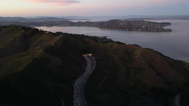 Evening commute traffic enters tunnel through coastal mountain at sunset