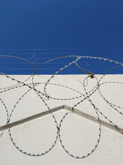 Barbed wire on white wall and blue sky. Abstractnaf photo with symmetry and shadows. High quality...