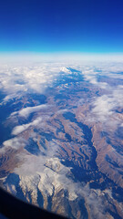 Fototapeta premium View from window of plane to blue sky and snowy mountain peaks in white clouds. High quality photo