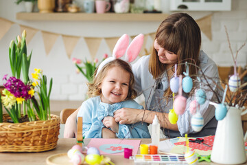 Obraz na płótnie Canvas Beautiful mother and cute daughter are spending quality time together, making craft handmade eggs for Easter home decoration. Spring flowers, cozy holiday atmosphere , family traditions and values