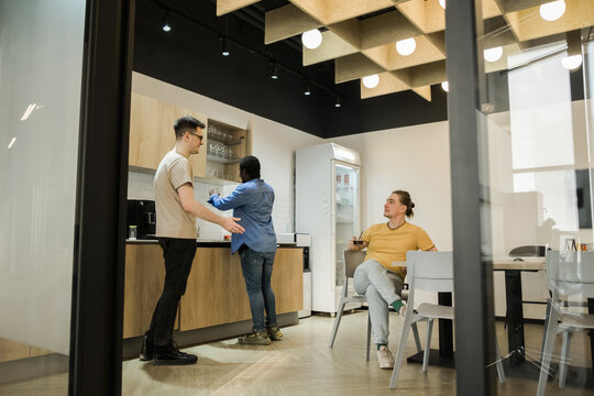 Group of cheerful young people talking and smiling during coffee break time in the office. Team of professional software developer relaxing in the canteen.