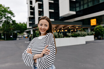 Lovely curt lady with happy smile wearied casual light clothes is smiling to camera with true happy emotions and enjoying ealing in the city in modern district