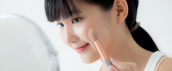Beautiful young asian woman applying brush on cheek makeup of cosmetic looking mirror on bed, beauty of girl with skin facial and wrinkle in the bedroom, cosmetology for female, skincare concept. - obrazy, fototapety, plakaty