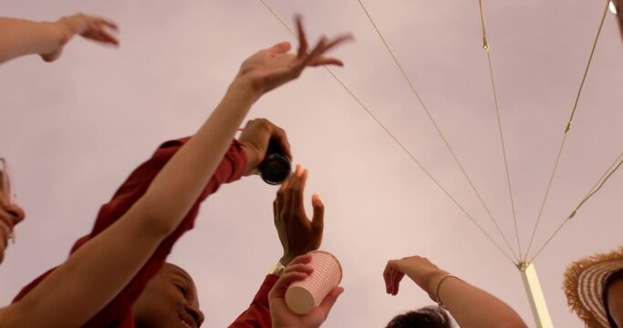 multi-ethnic happy people dancing with raised arms toasting with beer bottles at urban rooftop party at sunset, friendship party craziness, mena dn women have fun enjoy birthday outdoors slow motion