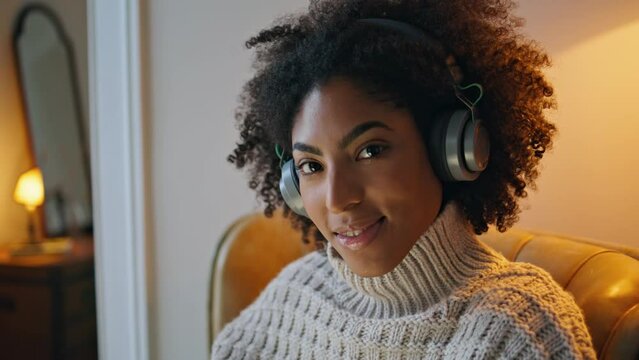 Headphones lady smiling camera armchair portrait. African woman enjoying music