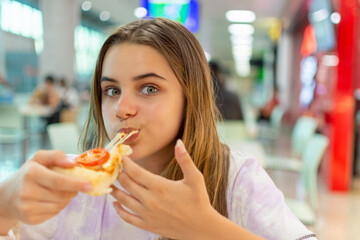 Menina adolescente comendo pizza com muito prazer