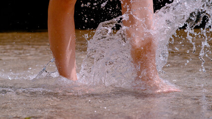 CLOSE UP: Water splashes while young barefoot woman crosses shallow alpine river