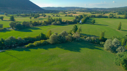 AERIAL: Charming Planina Karst Field with meandering river Unica on a summer day
