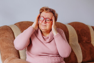 Overweight senior woman experiencing an aching headache, clutching her head with her hands at home,...