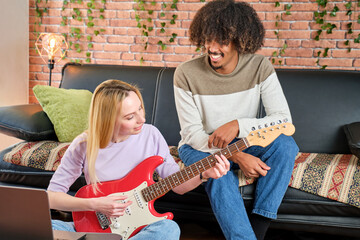 multiracial couple learning to play the guitar with tutorials on the sofa at home