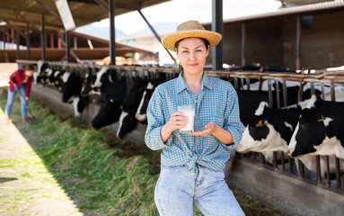Fototapeta na wymiar Portrait of a positive kazakh farmer woman standing in a cowshed, holding a glass of fresh milk in her hand