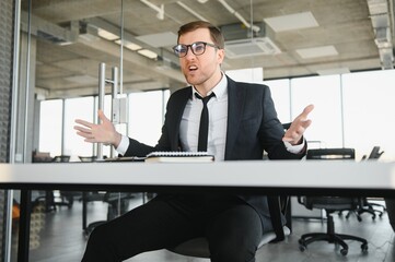 Angry senior businessman sitting at his desk and screaming