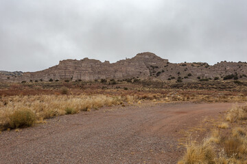 Desert mountain behind dirt road with green bushes and overcast sky