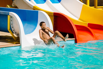 A little boy slides down a water slide and has fun. The boy swims in the pool after going down the water slide in summer.