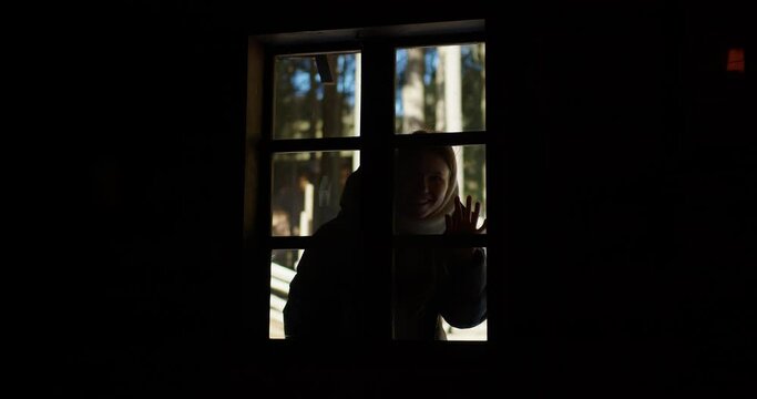 a girl in a white scarf looks into the window of an old house from the street. granddaughter goes to visit her grandmother in the village. a woman knocks on the window