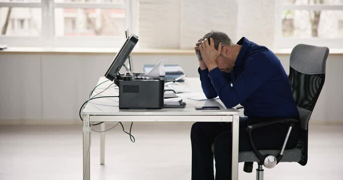 Irritated Businessman Looking At Paper Stuck In Printer