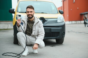 Man Holding Power Charging Cable For Electric Car In Outdoor Car Park. And he s going to connect the car to the charging station in the parking lot near the shopping center