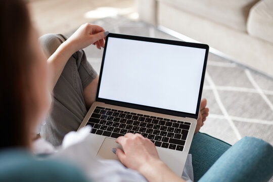 Mockup white screen laptop woman using computer sitting on armchair at home, back view, focus on screen