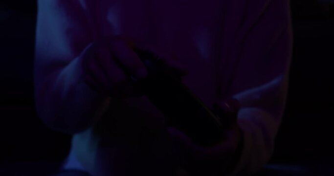 Detail of a woman's hands with a controller playing video games with colored lights