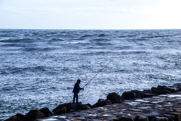 Man fishing on pier with rough sea. Stormy. 