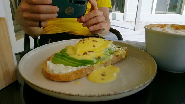a man takes pictures of his lunch on his phone - Eggs Benedict and a cup of coffee